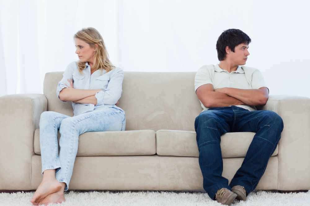 Man and woman on opposite ends of the couch with arms folded and looking away from one another