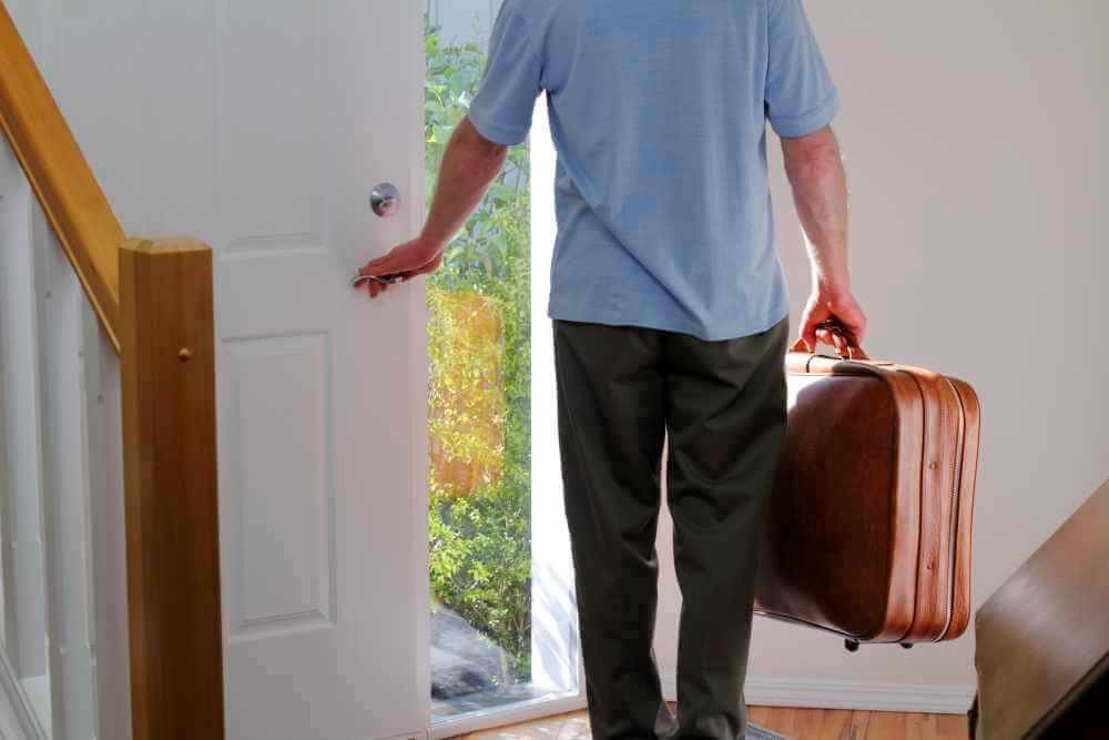 Man walking out the front door with a suitcase