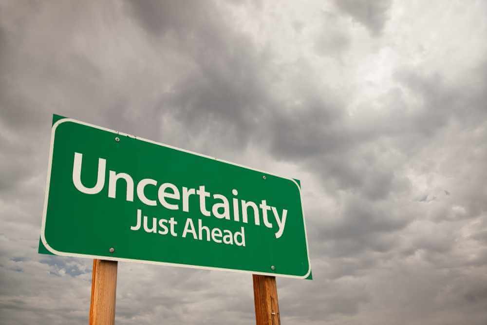 A road sign that says "Uncertainty: Just Ahead" against a dark clouded sky